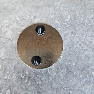 Round metallic object with two black knobs on a gray concrete surface
