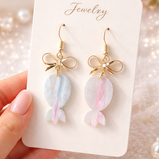 Pastel candy bow drop earrings with gold hardware on marble background